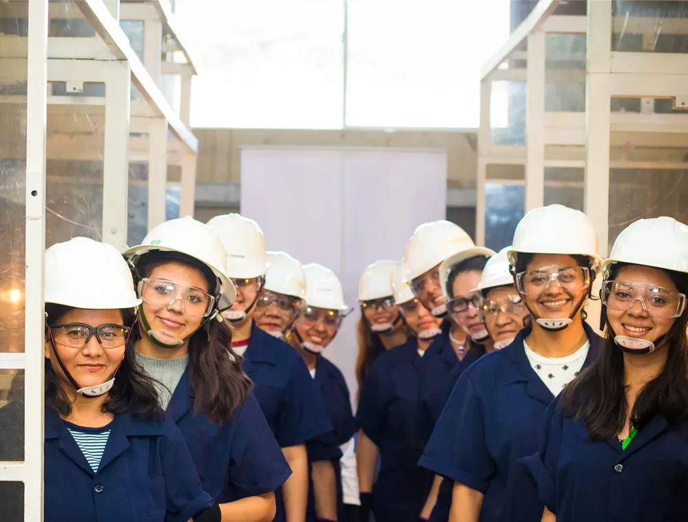 A group of people wearing safety helmets and goggles, standing in a line inside an industrial setting.