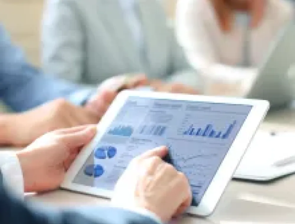 Person holding a tablet displaying financial graphs and charts during a business meeting.