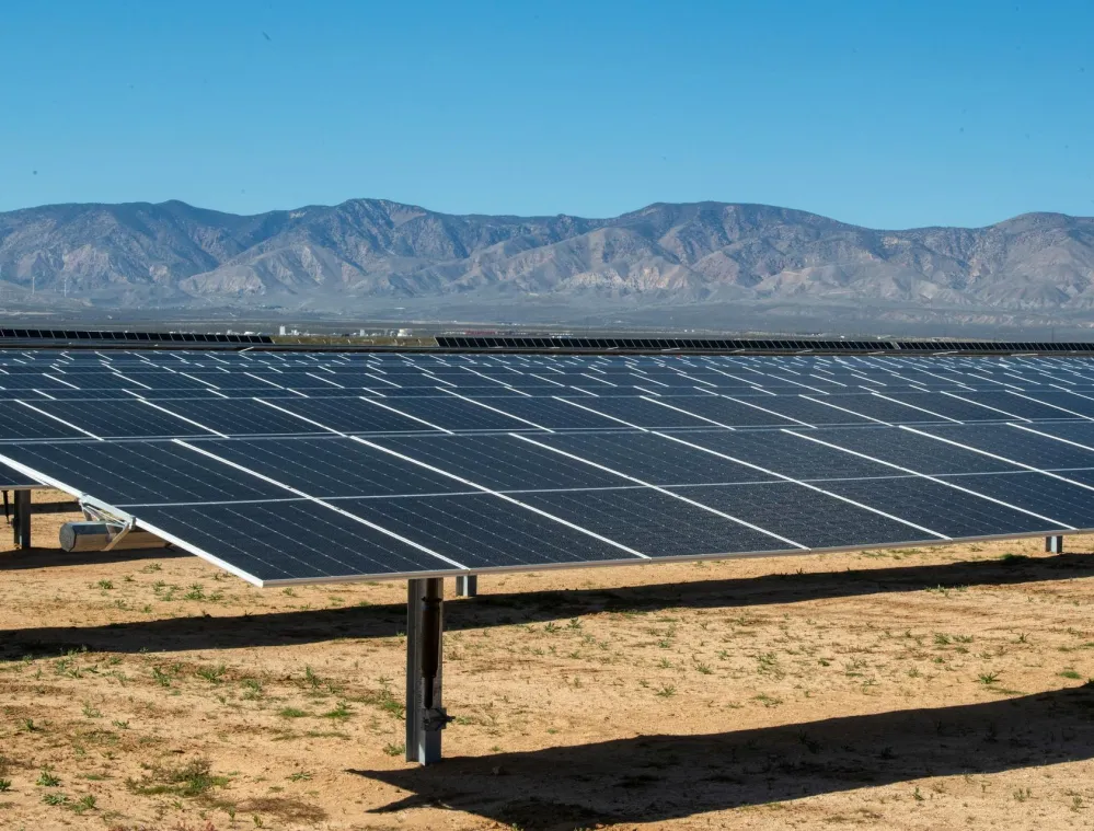 A field of solar panels on a desert landscape with mountains in the background under a clear blue sky.