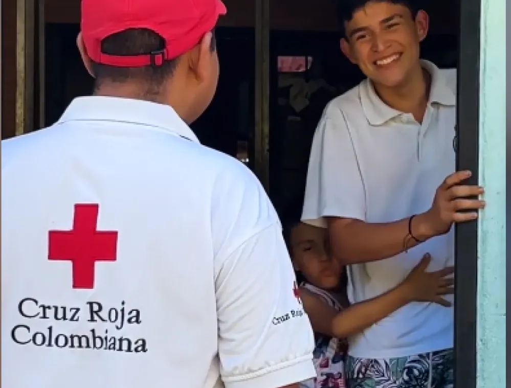 A Colombian Red Cross volunteer standing in a doorway talking to a smiling young man and a child.