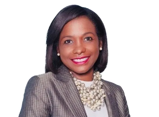 Smiling woman in a plaid blazer and pearl necklace on a white background.