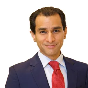 A person wearing a dark suit, white shirt, and red tie, smiling against a plain white background.