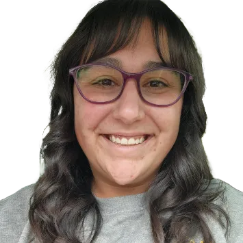 Jen Burfield deadshot. Smiling person with long dark hair and purple glasses, wearing a grey shirt.