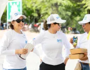 Three people wearing white shirts and caps with 'aes' logos, standing outdoors. One person holds gloves, another holds a juice box and two cardboard boxes. They appear to be smiling and conversing.